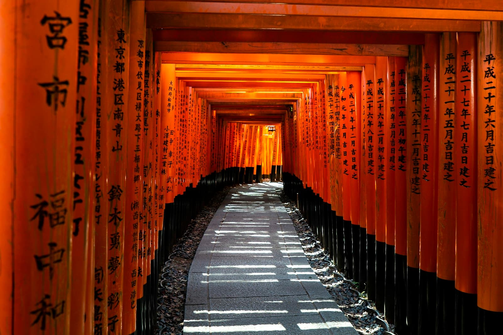 A stone path through a tunnel of orange torii gates at Fushimi Inari in Kyoto