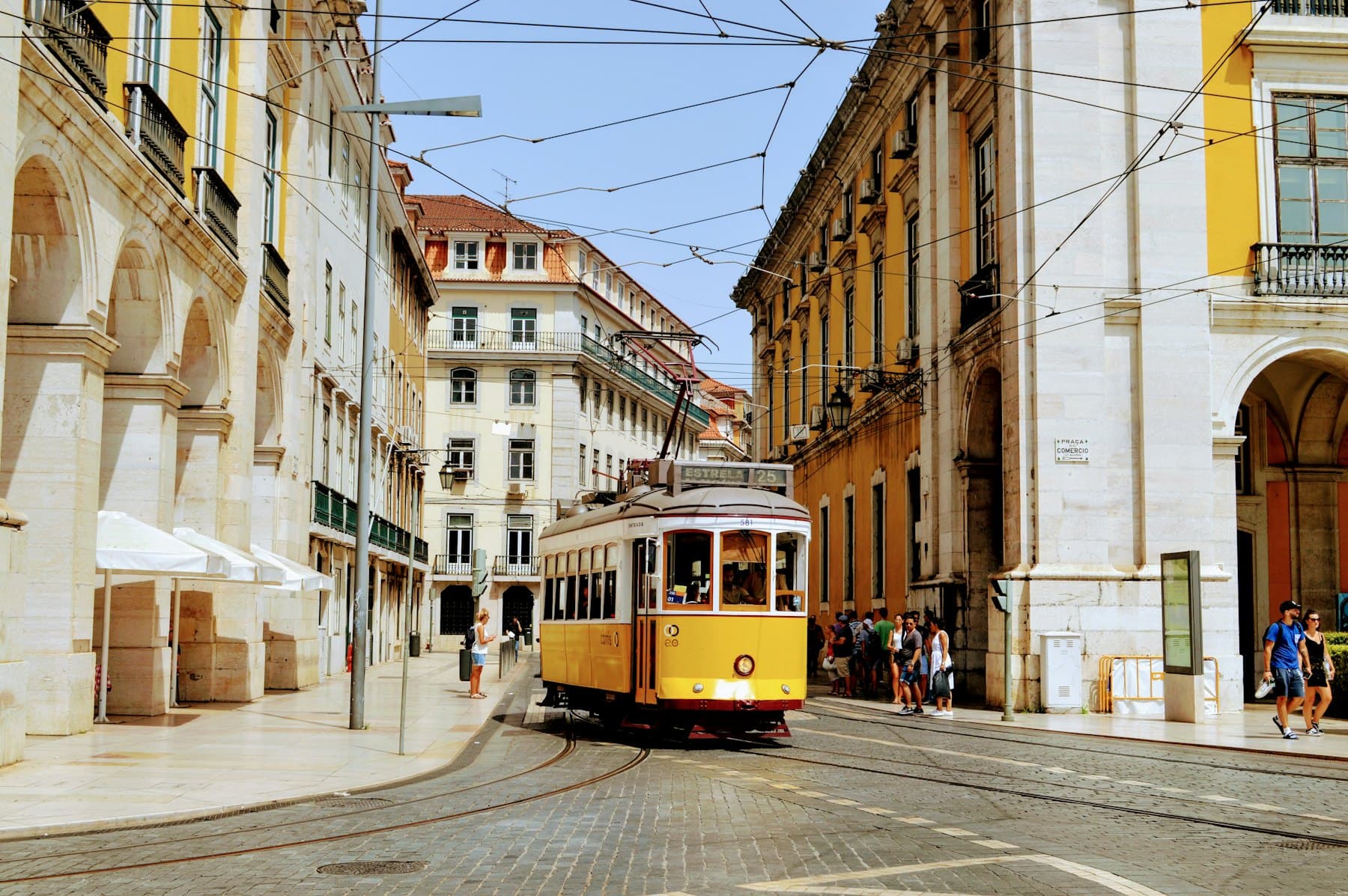 A yellow tram climbing a narrow street between tiled buildings in Lisbon